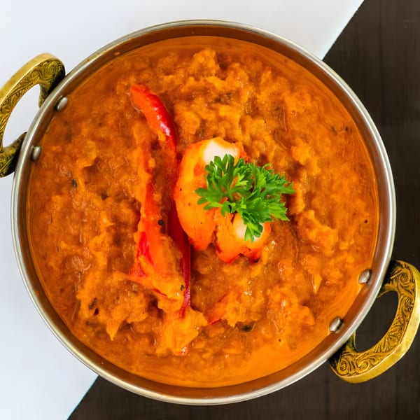 Bombay Kitchen's Indian curry in a brass-handled bowl, garnished with parsley and red pepper.