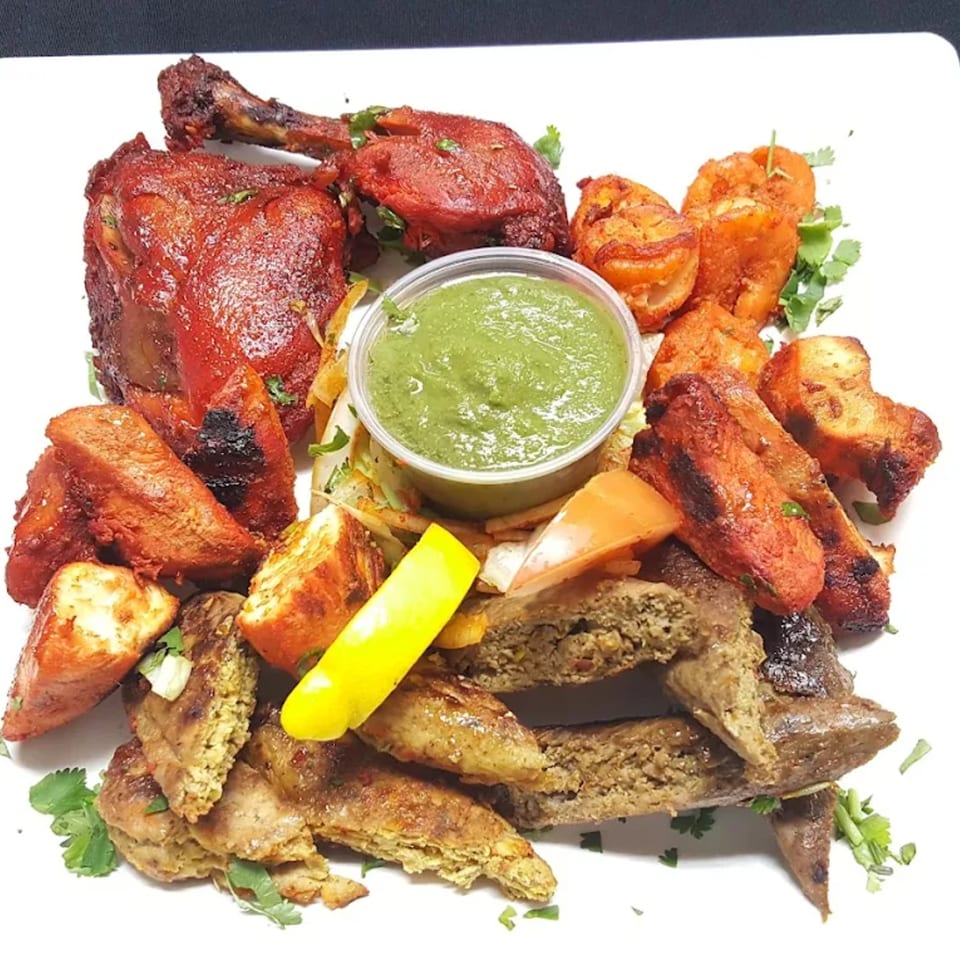 A platter of Indian cuisine including tandoori chicken, paneer, and seekh kebab with green chutney.
