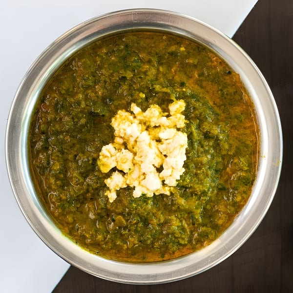 Palak Paneer, a vibrant green Indian spinach and cheese dish, served in a silver bowl.