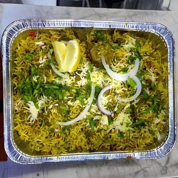 Bombay Kitchen's Indian biryani with rice, meat, onions, cilantro, and lemon wedges in a foil container.